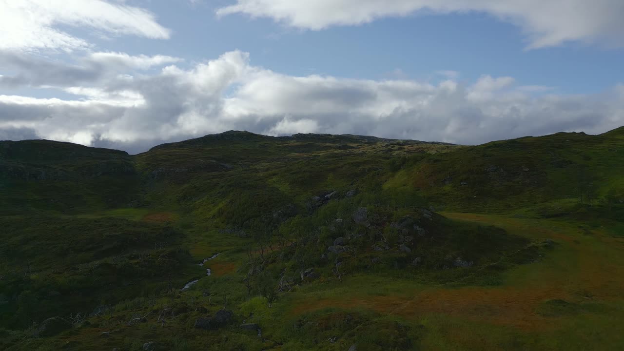 A drone soars over a picturesque hilly landscape, where a winding creek flows gently through vibrant fall-colored wetlands.