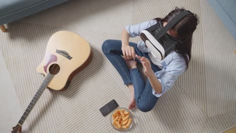 top view of asian teen girl sitting on carpet on the floor at home, touching air panel and swiping virtual reality with hand while using futuristic goggles