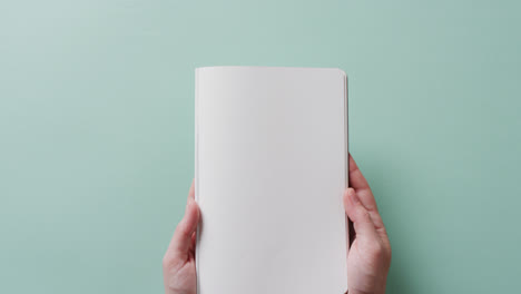 Close-up-of-hands-holding-book-with-copy-space-on-green-background-in-slow-motion