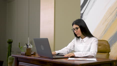 Serious-Business-Woman-Working-On-Laptop-Computer-And-Then-Writing-In-The-Agenda-While-Sitting-At-Desk-In-The-Office-1