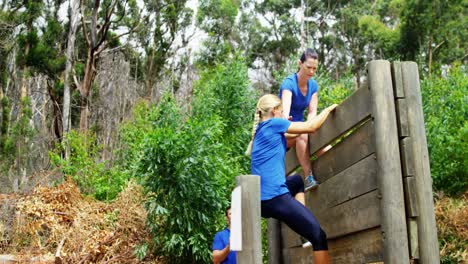 Trainerin-Hilft-Fitter-Frau-Dabei,-Während-Des-Hindernisparcours-4k-über-Eine-Holzwand-Zu-Klettern