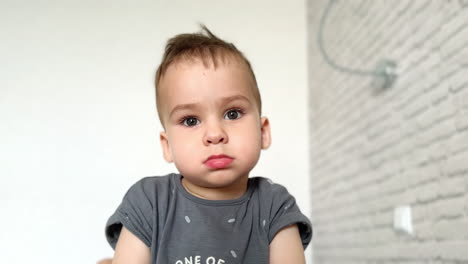 calm caucasian baby boy staying serious looking at camera. in a second kid starts to smile and jump. close up.