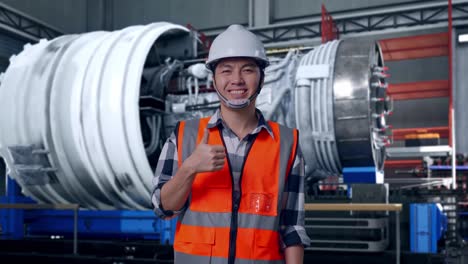 asian male engineer with safety helmet smiling and showing thumbs up gesture to the camera while standing with airplane engine maintenance conducted, analytics checking the turbine