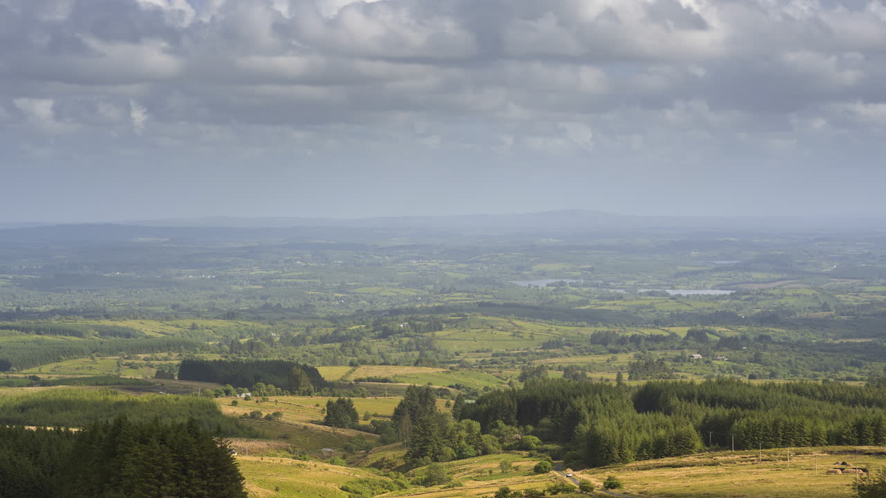lapso de tiempo del paisaje agrícola rural con campos y bosques en la distancia en un día nublado de verano en irlanda