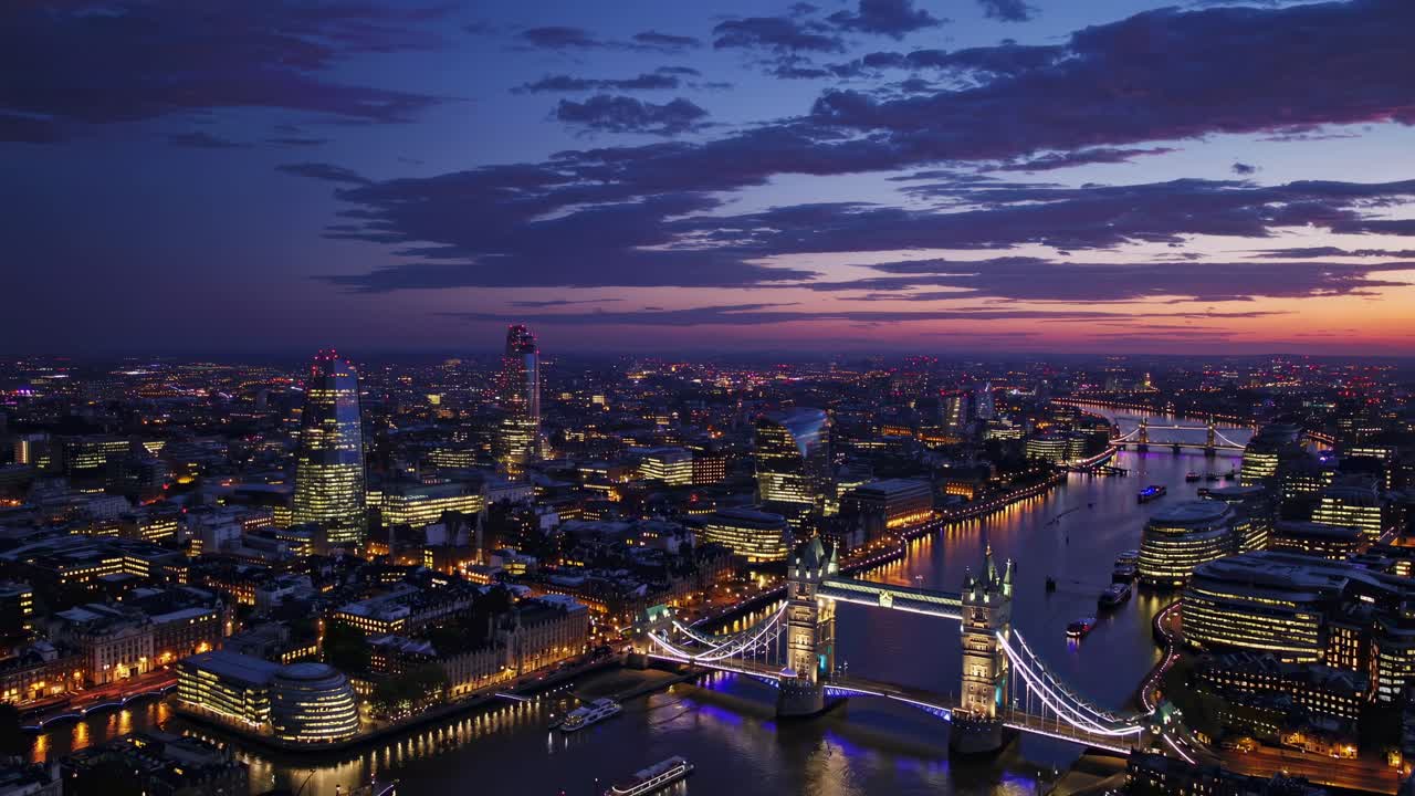 Aerial view of a cityscape at dusk, featuring illuminated bridges and skyscrapers