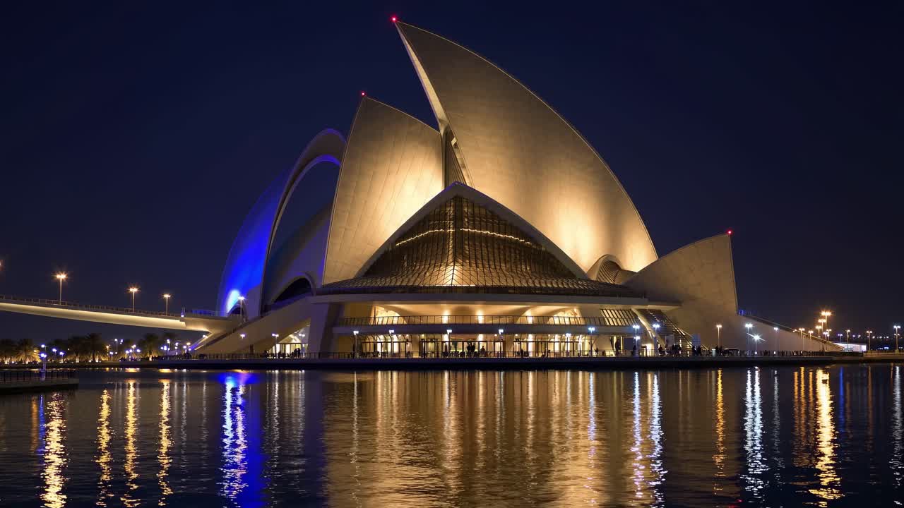 Dubai Opera's sleek architectural lines reflecting in nighttime waters, illuminated by surrounding city lights and bridging urban landscape, United Arab Emirates