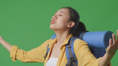 close up side view of asian female hiker with mountaineering backpack spreading arms enjoy looking the view around while standing on green screen background in the studio