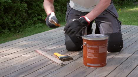 man in workwear put on work gloves and open and stir in a can of decking oil