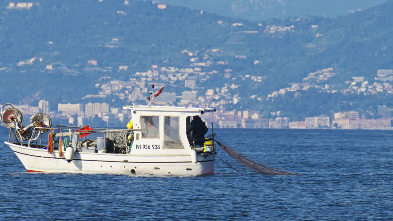 Antibes, Francia - 2 maggio 2025: vista di un uomo su una barca bianca che getta una rete da pesca nell'acqua blu in pieno giorno