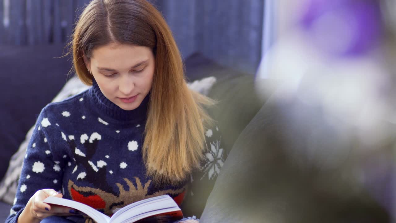 una joven lee un libro cerca del árbol de navidad.