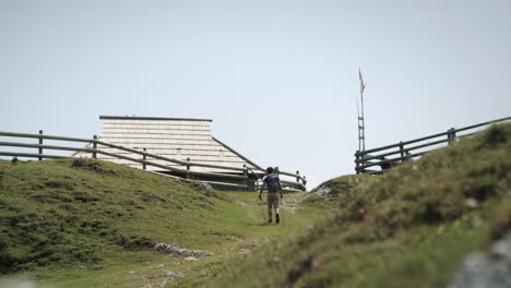 Una-Foto-De-Un-Excursionista-Caminando-Con-Una-Mochila-Y-Bastones-De-Senderismo,-Acercándose-Al-Pueblo-De-Montaña