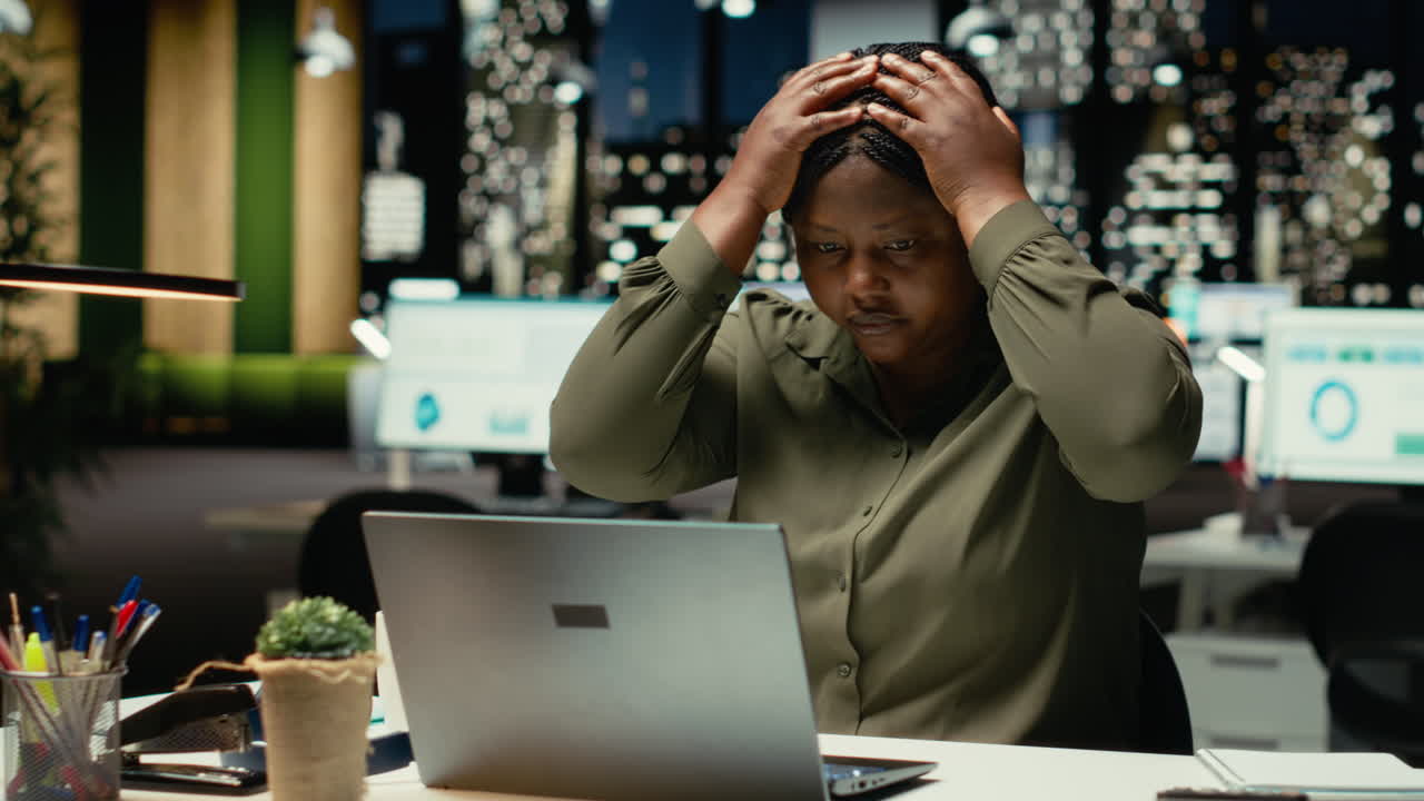 Black female assistant tensed and burdened in dark office after hours