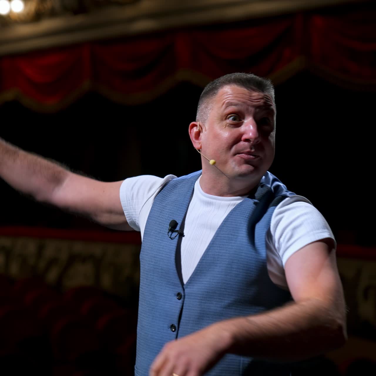 Man entertainer, presenter or actor on stage. Active gestures of throwing to the auditorium. View of a male public speaker speaking at the microphone, pointing in front