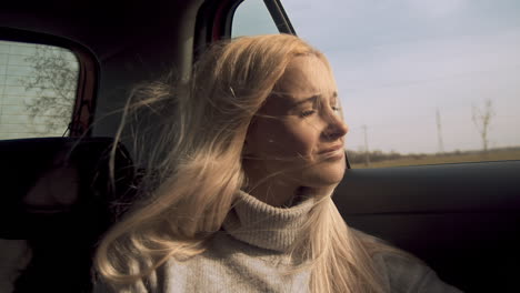 young blonde woman smiles out car window as wind blows hair, slow motion