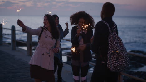 portrait-diverse-group-of-women-friends-waving-sparklers-dancing-happy-enjoying-new-years-eve-celebration-multi-ethnic-girlfriends-celebrating-birthday-on-evening-seaside-sunset