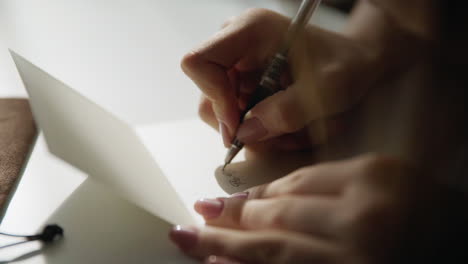 Beautiful-female-hand-writing-a-wedding-or-holiday-invitation-on-a-bright-white-table-with-candles