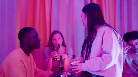 three multiethnic young friends spending time together, talking and drinking during a party at home