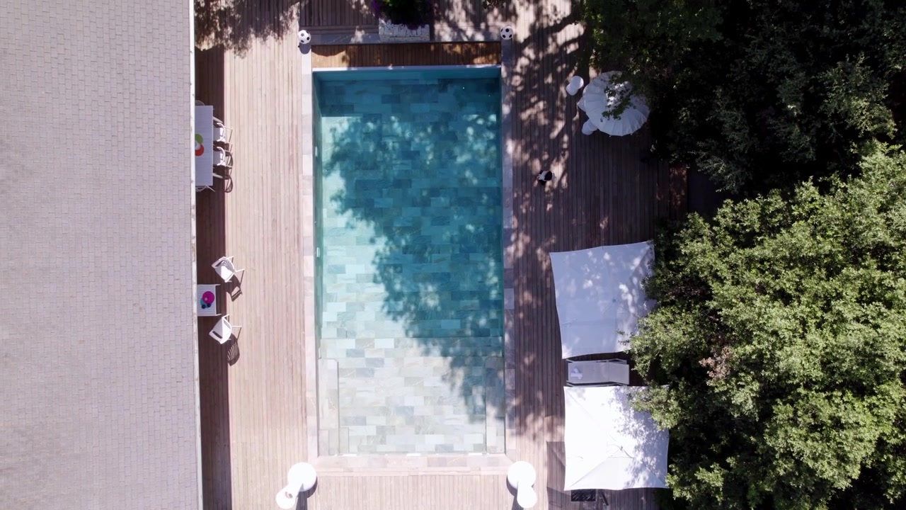 Aerial dolly shot overhead a woman walking at the poolside of a villa