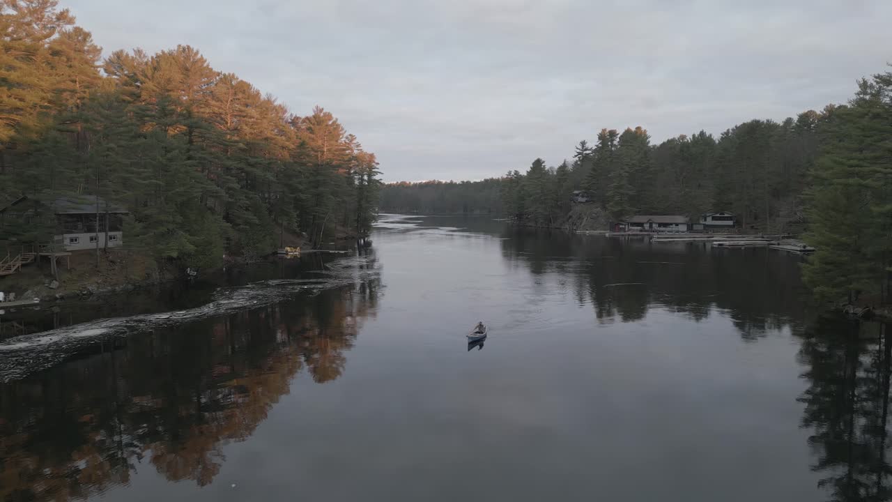 persona en canoa en un río tranquilo rodeado de orillas boscosas al amanecer, con reflejos de árboles en el agua