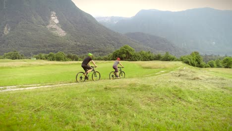 aerial view of a couple driving mountain bikes on dirt road surrounded by hills.