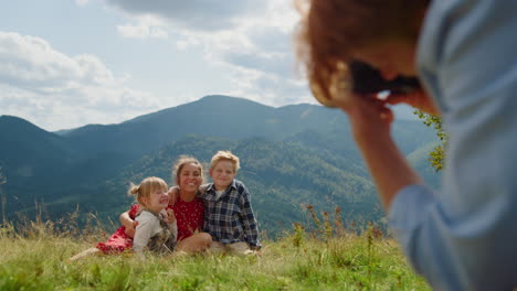 father taking photos family sitting grass mountain meadow. people enjoy summer.