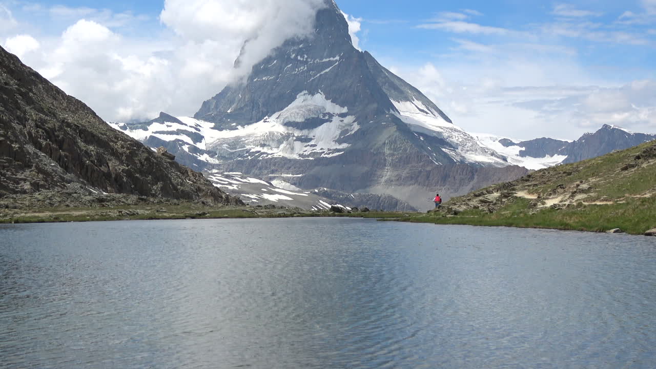 Ampia inquadratura di un lago alpino calmo con il Cervino che si erge sopra pendii rocciosi e nevai, nuvole estive che si muovono su Zermatt, Vallese, Svizzera.