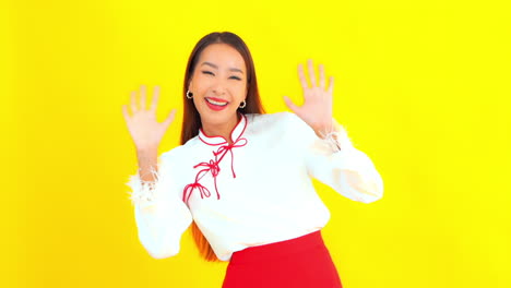 노란색 배경 앞에서 카메라를 향해 손을 흔드는 꽤 행복한 아시아 소녀