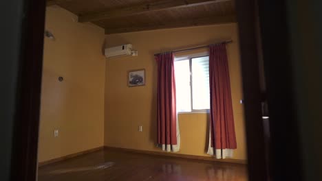Slow, left movement camera shot into yellow walled empty bedroom with reddish curtains and natural light coming in. Shot on 4K.