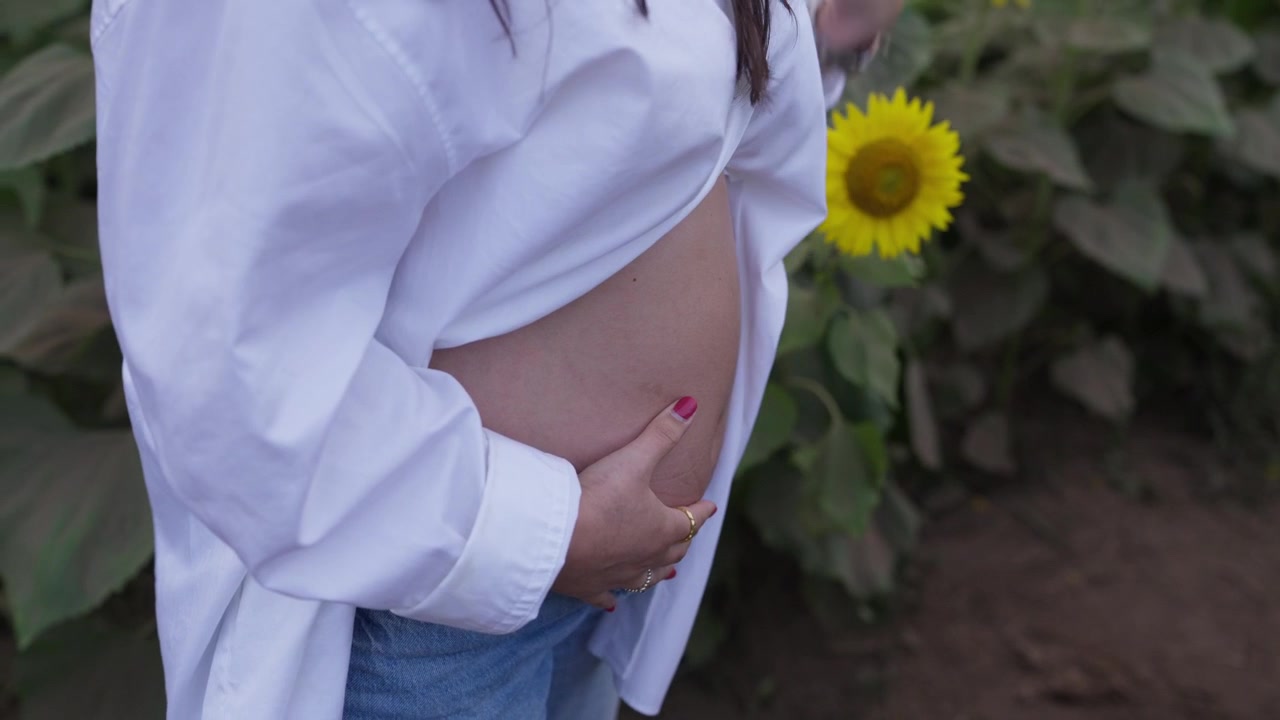Pregnant woman cradling her bare baby bump beside sunflowers in a field