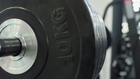 ten kilogram black bumper plates stacked tightly on chrome barbell sleeve reflect gym lighting while resting on rack, emphasizing weight load, textured rubber surface, engraved kg marking