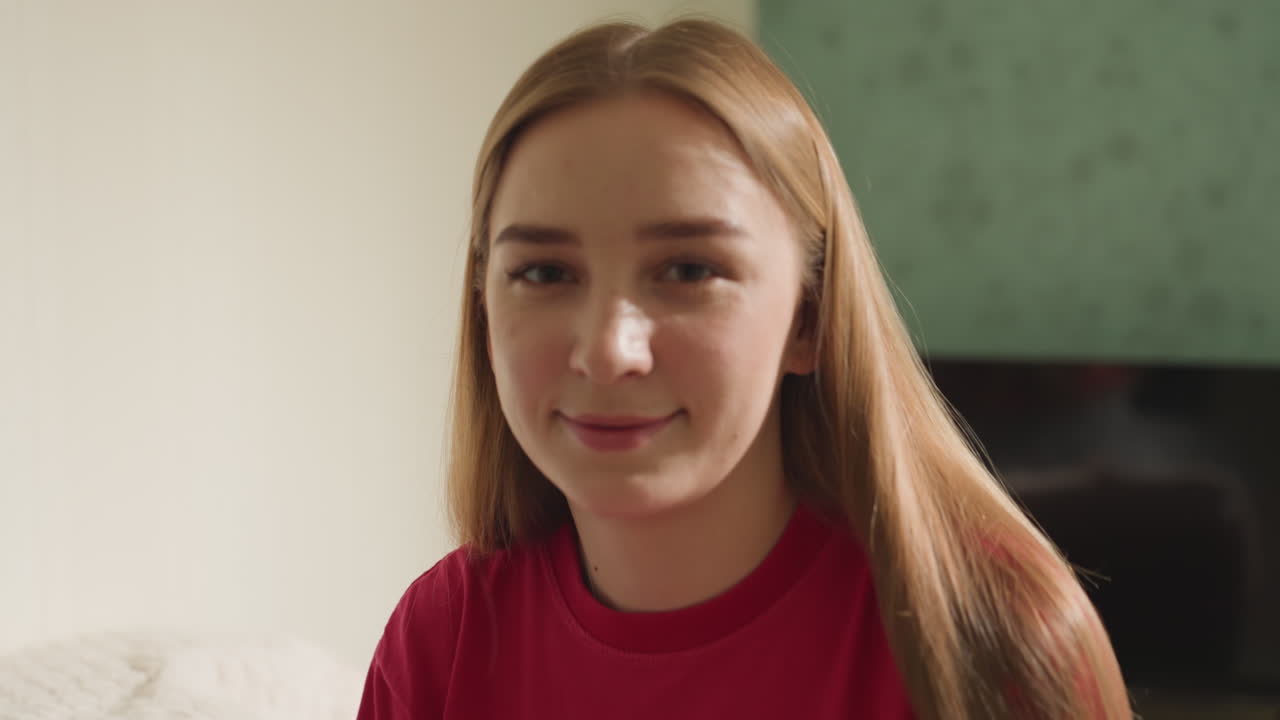 adolescente caucásica sonriendo mientras avanza su labor de punto en el sofá, expresión de felicidad tras dominar la puntada, lana roja y agujas visibles, ambiente cálido en el salón y energía estimulante de aprendizaje social