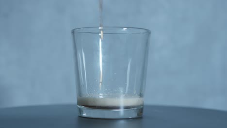 root beer soda flows into a small glass, creating a frothy crown at the top