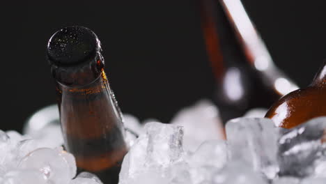 cerrar las botellas de vidrio de cerveza fría o refrescos que se enfrían en un cubo lleno de hielo contra un fondo negro 3