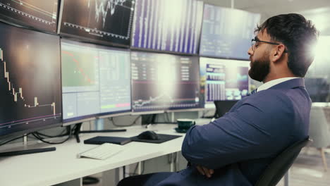 a businessman in a suit looking at financial data on multiple monitors in an office