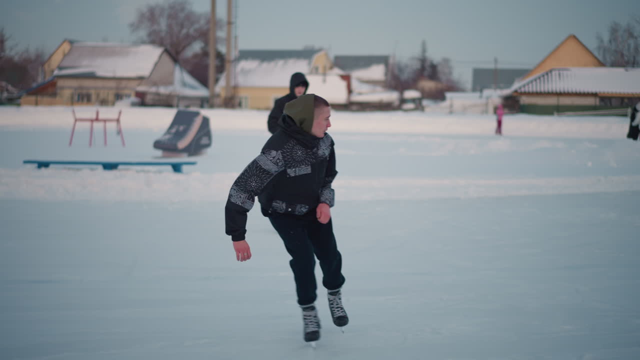 skater glides past group of ice skaters on frozen lake wearing winter gear skillfully weaving through others under pastel sky with snowy banks and residential houses in background