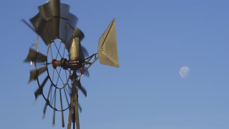 old windmill turning with the wind, with the moon in a bright blue sky, in patagonia, argentina