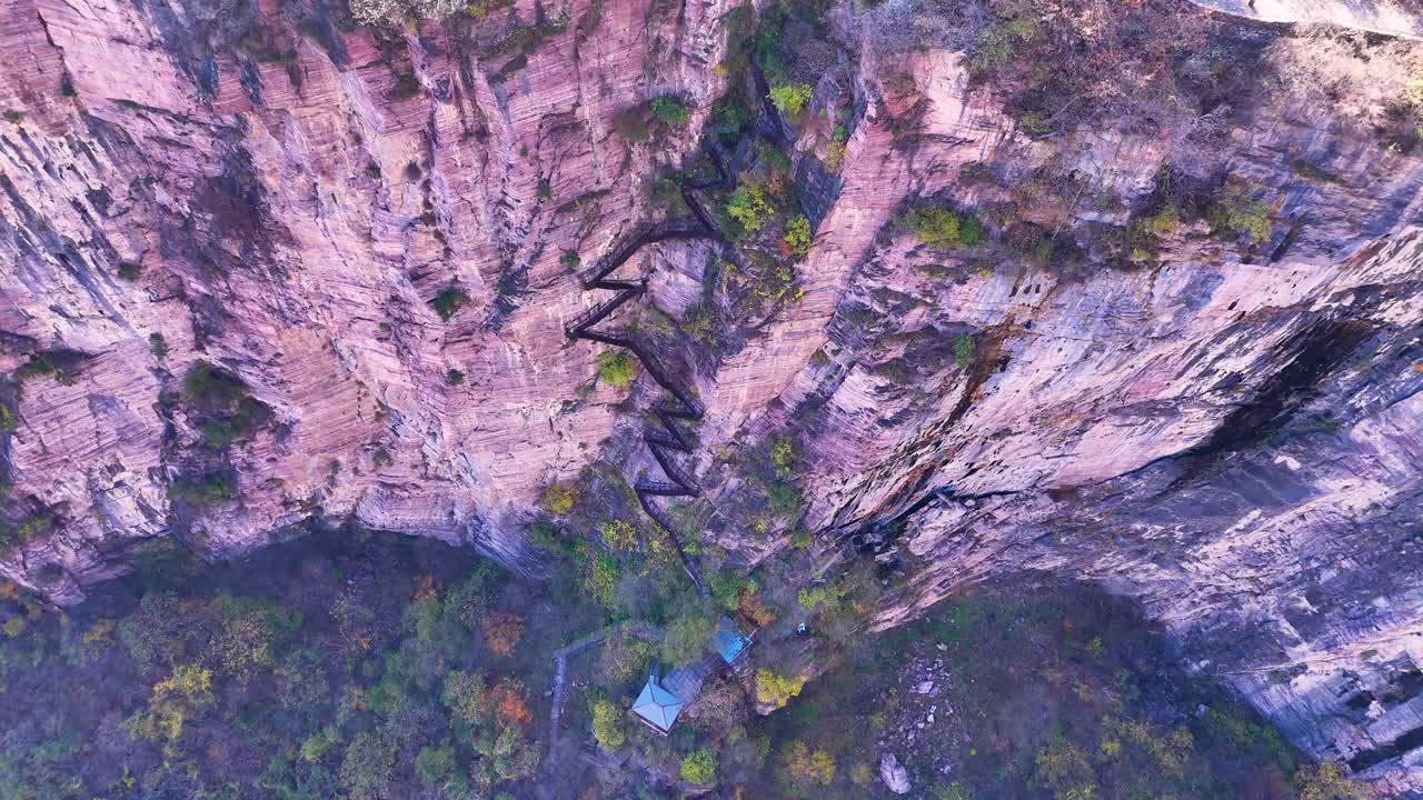 중국 제지안 지방 시우안 마을 근처의 바위 절벽에 새겨진 지그자그 계단을 위에서 아래로 내려다보며, 거친 자연의 아름다움과 인간의 기발함을 혼합합니다.