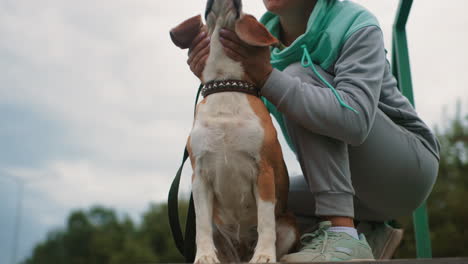 trainer holding mouth of her dog playfully while peaking him outdoors on wooden platform showing bond affection and playful connection between human and pet during relaxed casual moment