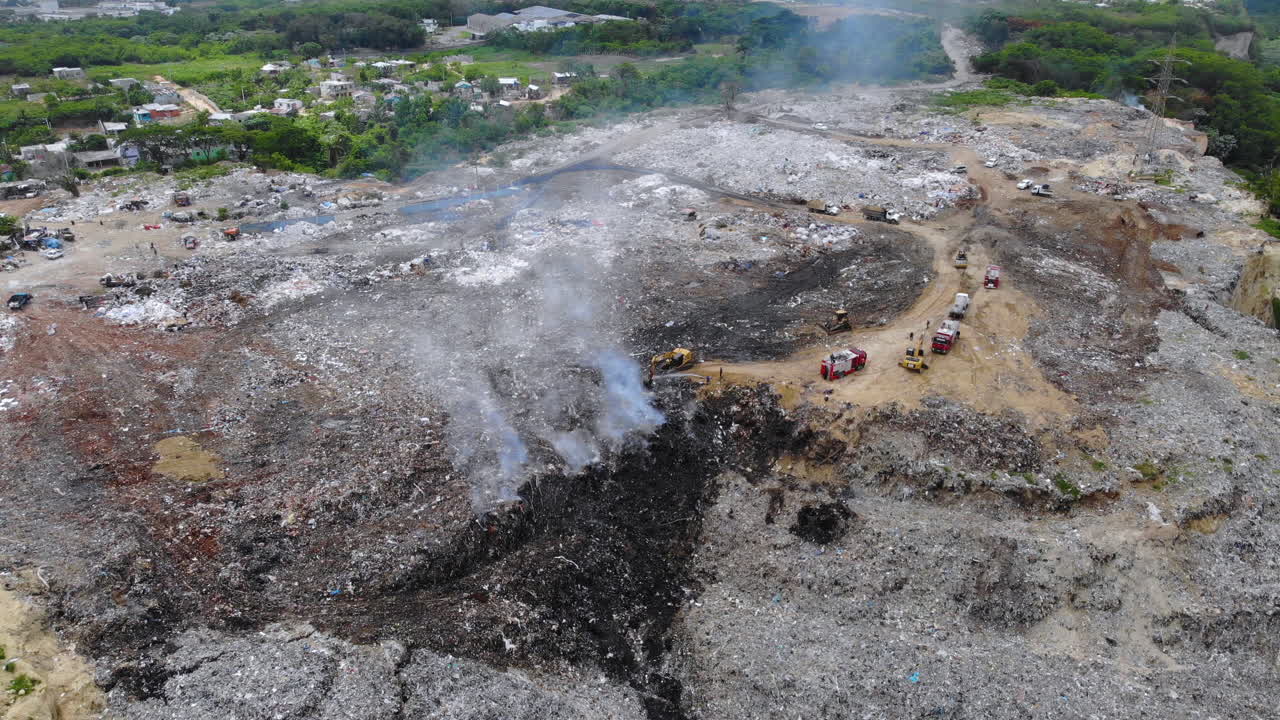 vista aérea de bomberos, combatiendo un incendio en un depósito de chatarra, humo saliendo en medio de montones de basura, en evento, santo domingo, república dominicana - tiro estático de drones