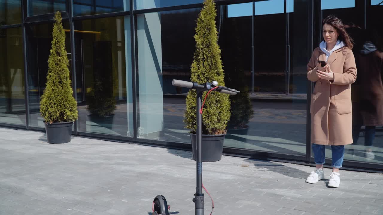 A young girl rents electric scooter using mobile phone app. Tourist phone application. Modern gadgets for young people and business people. Ecological city transport