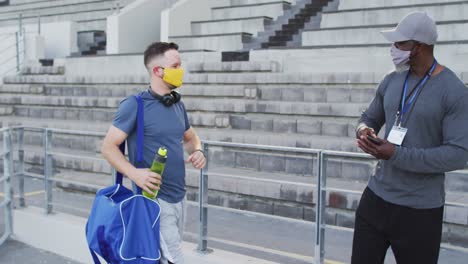 diverse male coach and disabled athlete wearing face mask touching elbows before training session