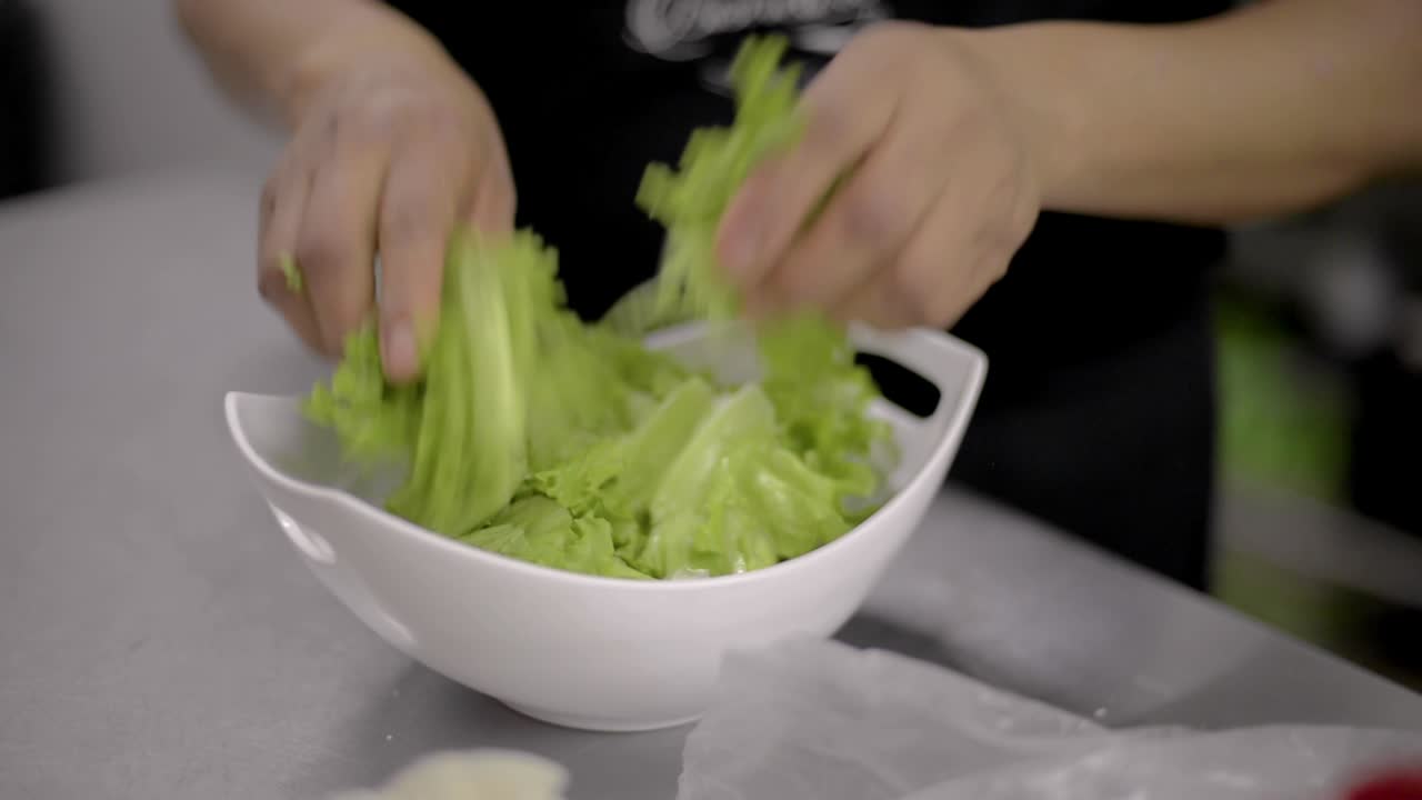 Woman chef cook preparing a salad tearing lettuce into a white bowl at a local restaurant diner cafe in Mexico latin america
