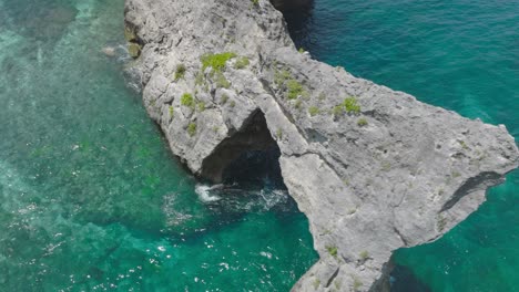 cinematic shot of famous rock arch on nusa batupadasan at atuh beach, aerial