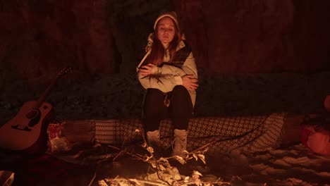 woman relaxing by a campfire in a cave at night