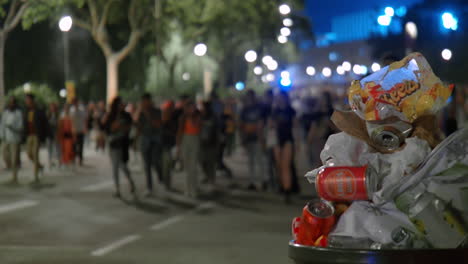 nightlife crowd walking past a trash can filled with empty cans and bags