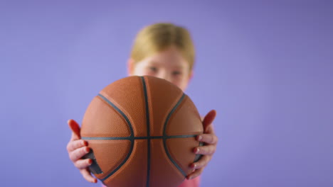 Foto-De-Estudio-De-Una-Joven-Sosteniendo-Baloncesto-Hacia-La-Cámara-Contra-Un-Fondo-Morado