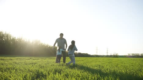 Happy-paternal-day-on-nature-with-daughters.-The-young-father-spends-time-in-fun-and-joy-with-the-children.-They-run-around,-play-on-a-beautiful,-green-meadow.-The-sun-is-shining