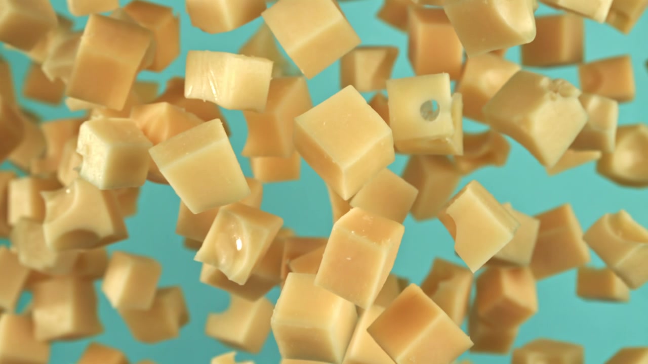 Cubes de fromage tombant au ralenti extrême sur fond bleu