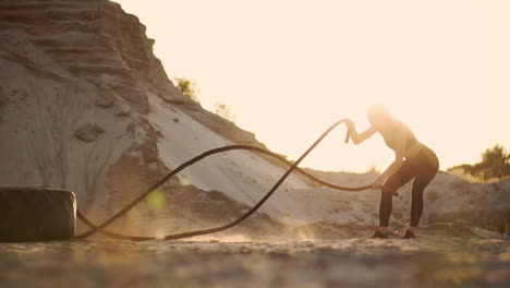 female athlete training outdoors around the sand hills at sunset. active physical activity workout. crossfit. the girl has a rope on the ground