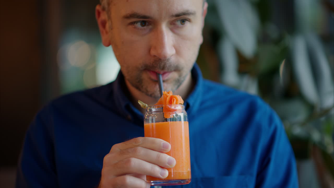 Man drinking carrot juice using of a straw, at a restaurant